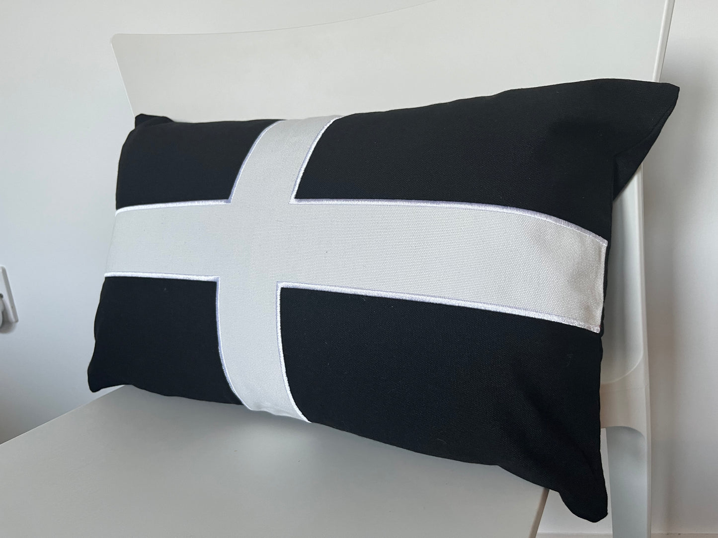 Cornish flag St Pirans flag cushion pillow with black and white cross design on a white chair.